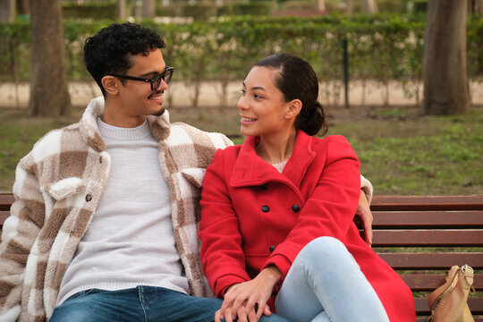 Happy couple holding hands and sitting on a bench in a park, enjoying time together