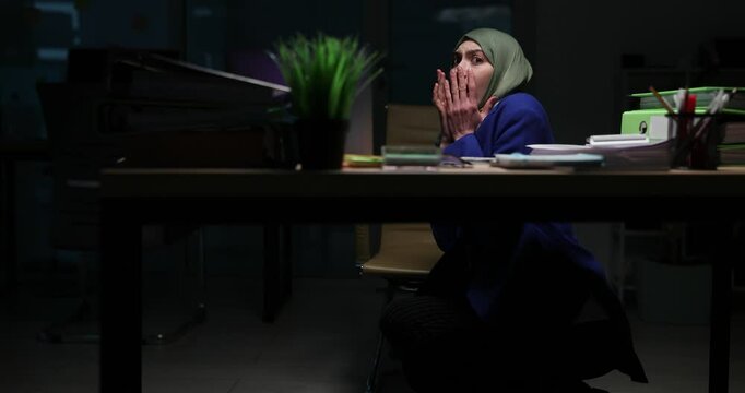 Frightened Muslim woman office worker hears sudden deafening rumble of thunder. Scared businesswoman clutches edge of desk in fear. Slow motion