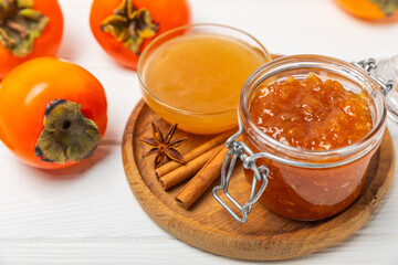 Persimmon jam with slices of ripe persimmon on wooden textured table. Delicious persimmon jam. Marmalade. Healthy sweets. Vegan. Close-up. Space for text. Copy space.