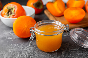 Persimmon jam with slices of ripe persimmon on wooden textured table. Delicious persimmon jam. Marmalade. Healthy sweets. Vegan. Close-up. Space for text. Copy space.