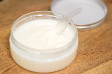 A jar of cream or coconut oil with a spoon on a wooden tray, ideal for face, body, and hair care, providing nourishment, hydration, and spa treatments.
