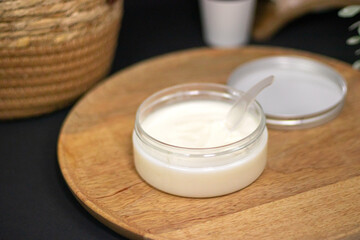 A jar of cream or coconut oil with a spoon on a wooden tray, ideal for face, body, and hair care, providing nourishment, hydration, and spa treatments.