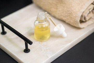 A serum bottle on a marble tray with a soft towel, set against a black background and wooden elements,  face care, hydration, nourishment, and spa treatments, promoting skin health and beauty.
