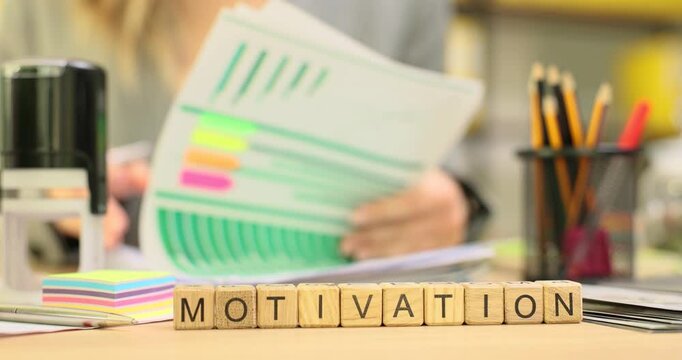 Office worker studies stack of documents on desk. Word MOTIVATION on cubes serves as reminder of importance of staying inspired at work. Slow motion