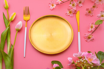 Golden plate with cutlery and spring flowers creating a beautiful table setting on a pink background, perfect for celebrating special occasions or enjoying a springtime meal