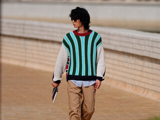 Portrait of handsome Chinese young man with striped sweater walking in the street, young guy with black curly hair with urban background. male fashion, cool Asian young man lifestyle.