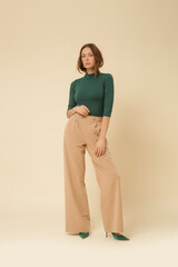 Obraz premium Series of studio photos of young female model wearing simple beautiful outfit, green turtleneck top and beige wide leg trousers