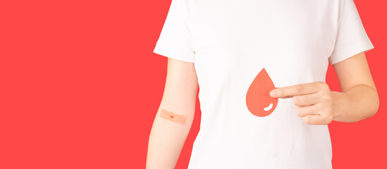 Blood donation. Human hands holding blood drop shape with plaster heart on arm against red...