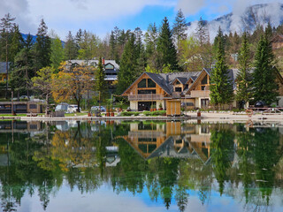 Obraz premium Wooden hotel reflecting on calm jasna lake waters, framed by lush greenery and julian alps in scenic kranjska gora, slovenia