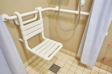 A bathroom with a chair in the shower in the hospital, designed for the disabled and people with disabilities, with tiled floors and walls. High quality photo