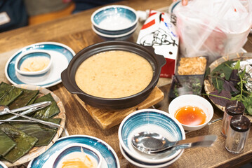 Flat chewy tapioca dumpling banana leaves wraps with large bowl rice soup, small dishes, dipping sauce, bamboo mat, traditional Hue dinner set, authentic Vietnamese cuisine balanced eating