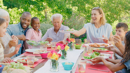 Multi-Generation Family With Friends Sitting Around Outdoor Table In Garden Enjoying Meal Together