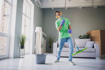 Young man enjoying household cleaning at home with a cheerful attitude in a well-lit living room,...