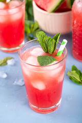 Homemade watermelon lemonade, sweet refreshing summer drink, iced watermelon juice with mint decor and striped straw, light blue and wooden background, copy space 