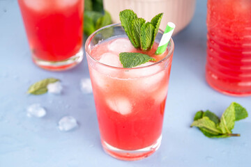 Homemade watermelon lemonade, sweet refreshing summer drink, iced watermelon juice with mint decor and striped straw, light blue and wooden background, copy space 