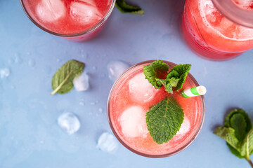 Homemade watermelon lemonade, sweet refreshing summer drink, iced watermelon juice with mint decor and striped straw, light blue and wooden background, copy space 