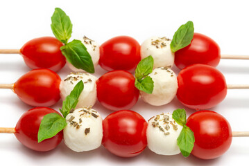 Caprese skewers with cherry tomatoes and basil leaves on a white background