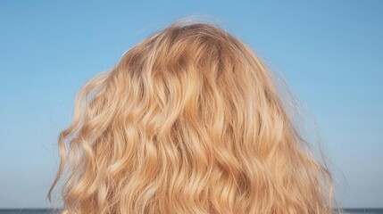 Naklejka premium Close-up of the back of a woman's head. the hair is long and wavy, with a golden blonde color. the background is a clear blue sky and the ocean can be seen in the distance.
