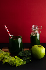 Vertical image of spinach, celery and green apple juice in a glass cup on a black background with red. Natural and healthy drink