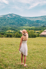 Young Blonde haired Woman in white dress walking on the green grass of Southern France, in front of Mountains