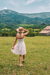 Young Blonde haired Woman in white dress walking on the green grass of Southern France, in front of Mountains