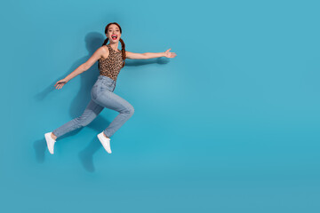 Energetic young woman in trendy leopard top and jeans posing joyfully against a vibrant blue...