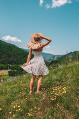 Young Blonde haired Woman in white dress walking on the green grass of Southern France, in front of Mountains
