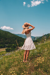 Young Blonde haired Woman in white dress walking on the green grass of Southern France, in front of Mountains
