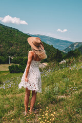Young Blonde haired Woman in white dress walking on the green grass of Southern France, in front of Mountains