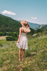Young Blonde haired Woman in white dress walking on the green grass of Southern France, in front of Mountains