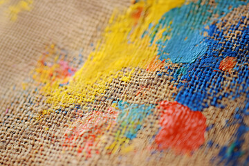 Fototapeta premium Close-up of textured jute fabric with colorful paint splashes