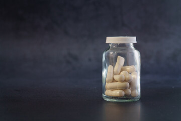 Medical Capsules in Transparent Glass Bottle on Dark Background