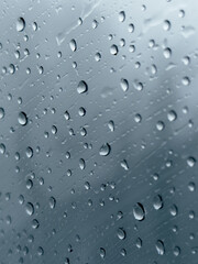 Close up of drops of water on the glass window with grey environment outside. Abstract vision of grey and rainy weather