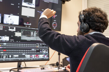 A television director in a broadcast control room, actively guiding a live production. Surrounded...