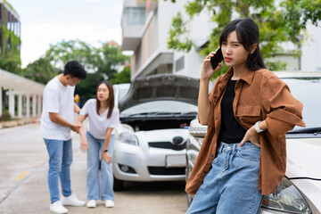 Fototapeta premium Asian Woman drivers call insurance after a car accident before taking pictures and sending insurance. Car Accident Emergency, while another person tends to a passenger with an injury.