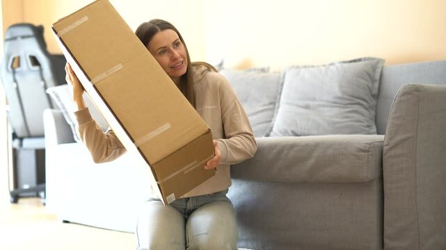 Excited young woman opens a package, removes packing materials, and finally discovers her long-awaited item. Pure joy of unboxing and surprise! Perfect for delivery and e-commerce themes.