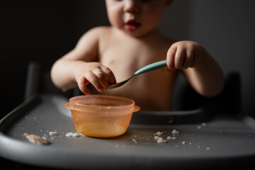 Little boy eating with rubber spoon learning how to eat in kitchen as eco family and eating skills. Developing eating skills with utensils 