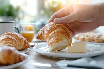 A close-up view of a hand picking up a flaky croissant with a generous slice of butter, showcasing the inviting texture and comfort that fresh pastries offer during breakfast or brunch.