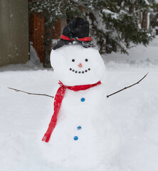 A large snowman with a red scarf, top hat and buttons stands in a snow covered yard.