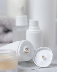 White cream tubes and bottles with open cap and beige scrub squeezing on table closeup