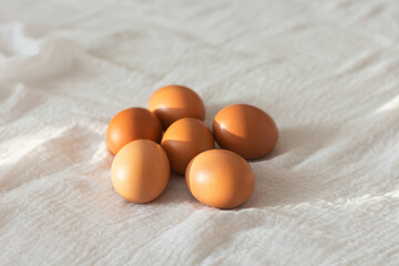 a few fresh brown chicken eggs lying on a white tablecloth.