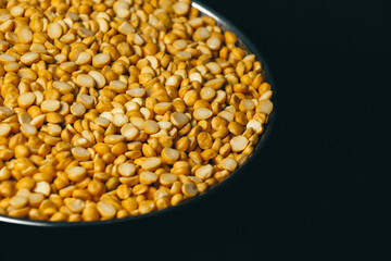 Closeup of Organic Bengal Gram (Cicer arietinum) on a steel plate against a black background with yellow chana dal.