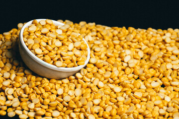 Close-up shot of Organic Bengal Gram (Cicer arietinum) placed in a ceramic white bowl, with split yellow chana dal forming the gradient background.