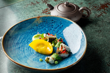 A beautifully plated gourmet dish featuring colorful dumplings, garnished with fresh herbs and delicate accompaniments, set against a rustic backdrop and a teapot.