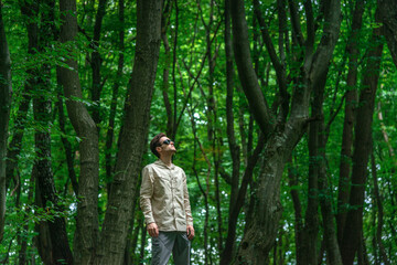 Adventurous man hiking in a forested mountain area, looking up. Sunlight filters through lush green...
