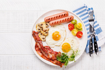 A classic breakfast plate featuring sunny-side-up eggs, crispy bacon, sausages, and fresh tomatoes