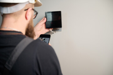 Security alarm installation. Security technician installing safe monitor on wall in the new office. Installing security system. Man worker installing alarm technology insurance in home
