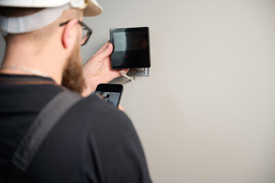 Security alarm installation. Security technician installing safe monitor on wall in the new office. Installing security system. Man worker installing alarm technology insurance in home