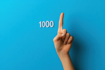 Woman pointing at number one thousand on blue background