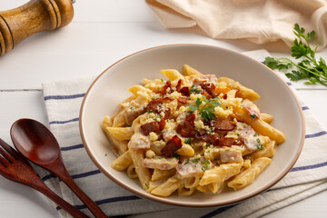 Creamy Penne Pasta Carbonara sauce bacon topped with parmesan cheese and crispy bacon in white plate.